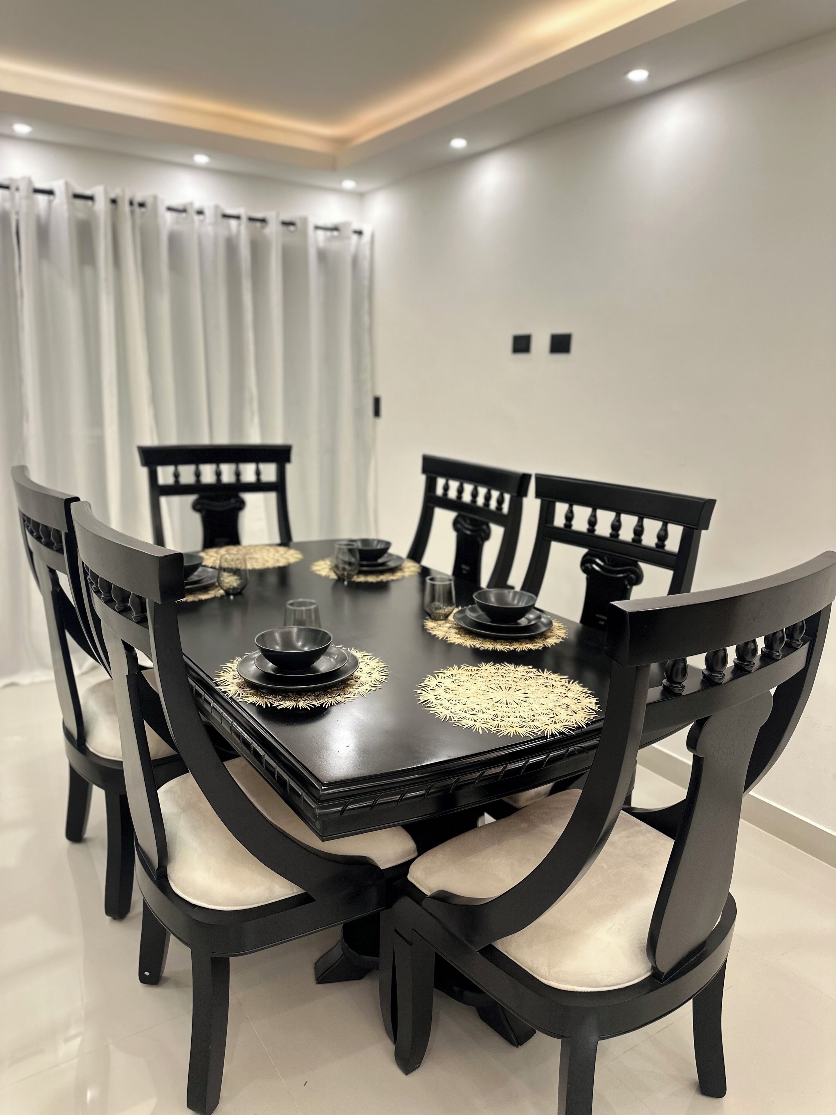 A dining room with a black table and chairs, white curtains, and recessed ceiling lighting.