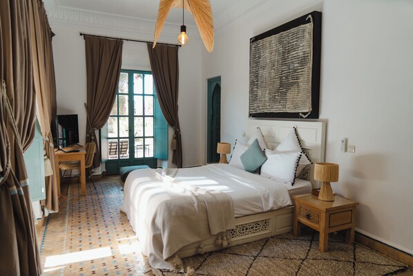 Une chambre à coucher avec un lit, des tables de chevet, un bureau et une fenêtre avec des rideaux.