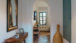 A hallway with a wooden console table, a large mirror, a wicker vase, and a window with decorative iron bars. - Villa-Riad with Private Pool in Marrakech, Akhdar 1 (Marrakech)