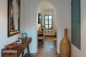 Un couloir avec une console en bois, un grand miroir, un vase en osier et une fenêtre ornée de barreaux en fer décoratifs.