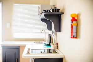 A kitchen with a built-in stove, a sink, a window with blinds, and a fire extinguisher mounted on the wall. - Room-makay's Guests House (Kimberley)