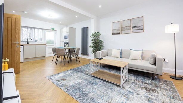 A modern living room with a sofa, coffee table, and dining area. - Entire Home Next to Trafford Centre (Stretford)