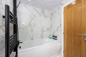 A bathroom with a marble wall, a bathtub, a wooden door, and a towel rack. - Entire Home Next to Trafford Centre (Stretford)