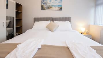 Un letto rifatto con lenzuola bianche, una coperta beige e due accappatoi bianchi piegati sopra il letto.