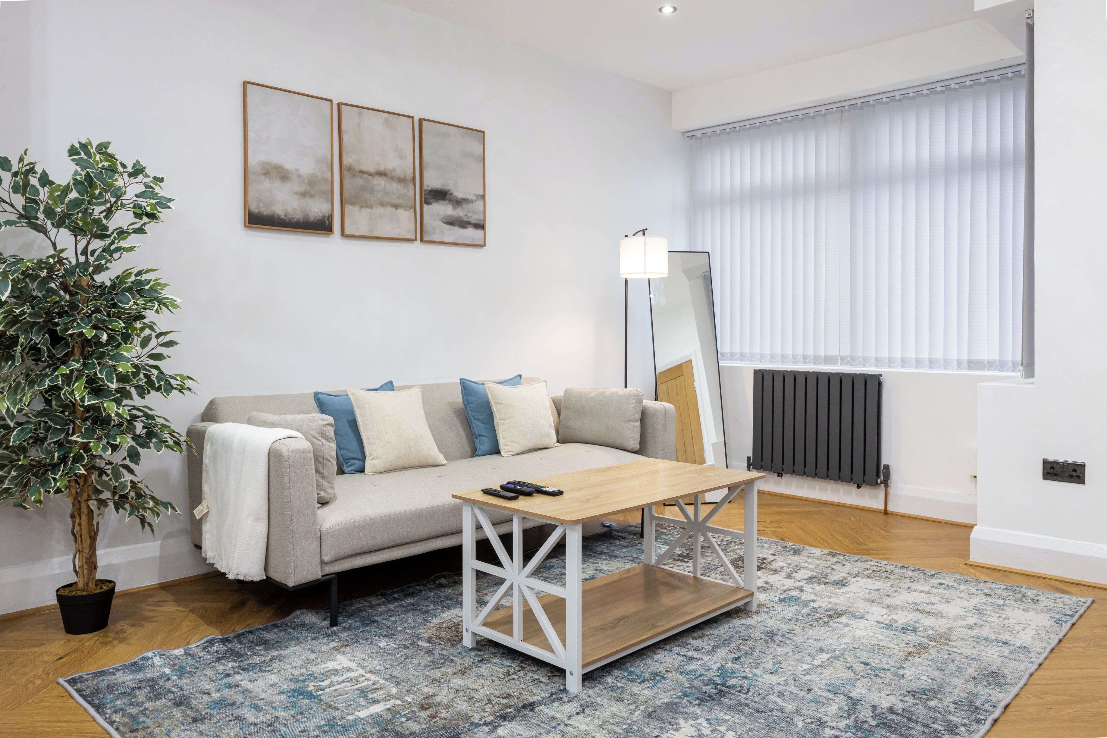 A modern living room with a sofa, coffee table, floor lamp, potted plant, and artwork on the wall.