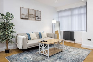 A modern living room with a sofa, coffee table, floor lamp, potted plant, and artwork on the wall. - Entire Home Next to Trafford Centre (Stretford)