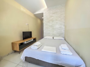 Ein Schlafzimmer mit einem Bett, einem Fernseher auf einem Holzboden und einer Wand mit Steinoptik.