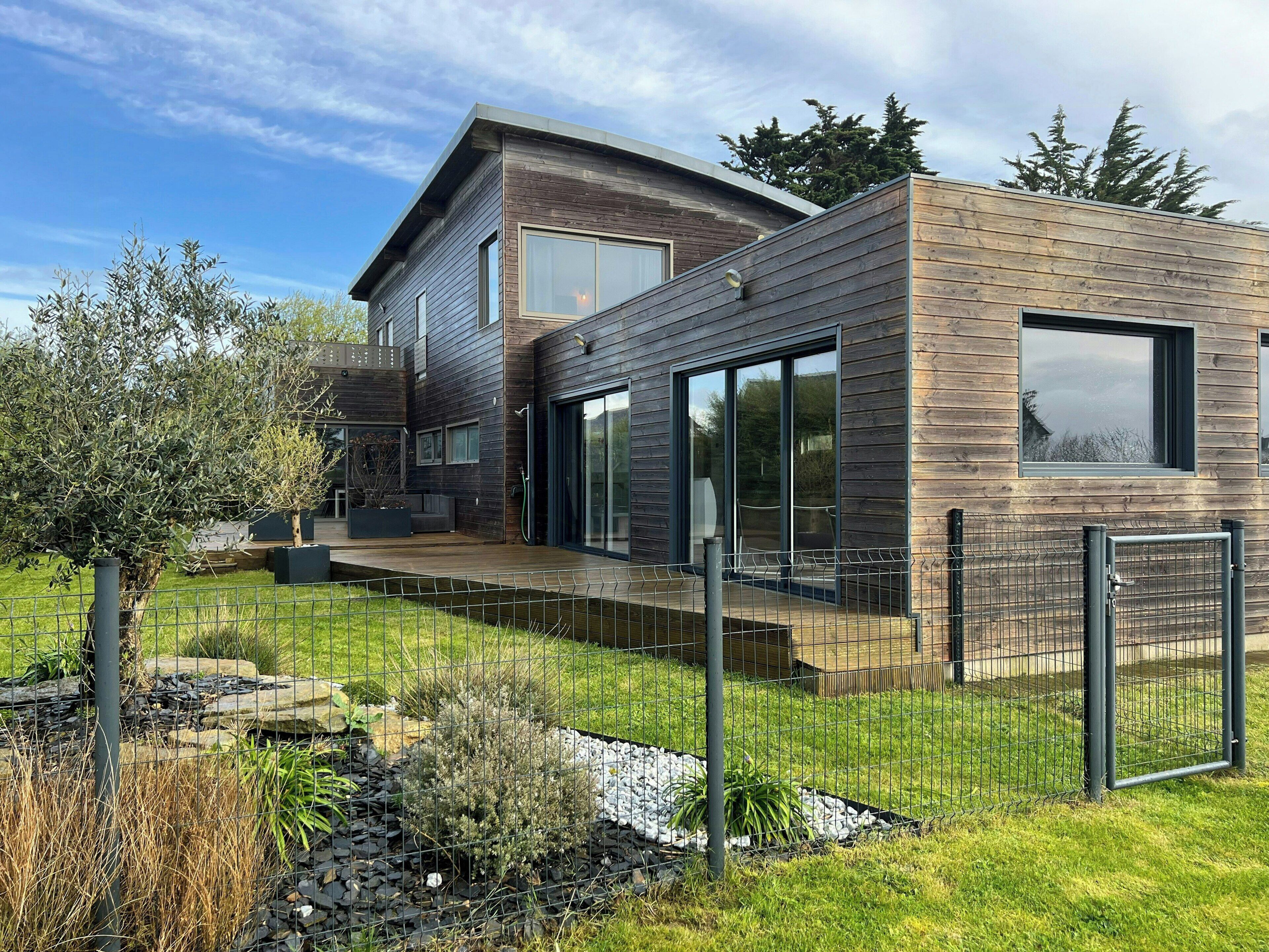 Ein modernes, zweistöckiges Haus mit Holzfassade, großen Fenstern und einem angelegten Garten.