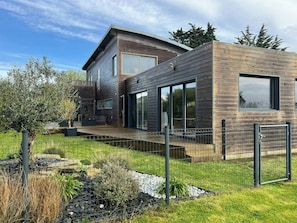 Ein modernes, zweistöckiges Haus mit Holzfassade, großen Fenstern und einem angelegten Garten.
