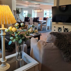 Sala de estar com sofá, mesa de centro, luminária e televisão. Escada leva a outro cômodo.
