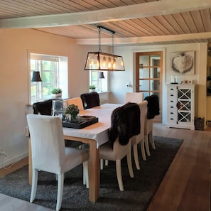 Uma sala de jantar com uma mesa de madeira, cadeiras brancas, um candelabro e um armário com gavetas.