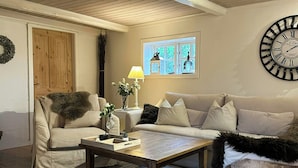 Un salon avec un plafond en bois, un ensemble de canapés, une table basse et une horloge murale.