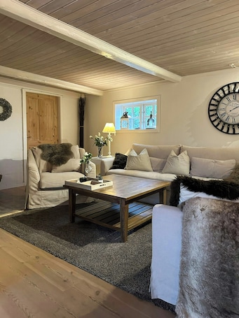 A living room with a wooden ceiling, a sofa set, a coffee table, and a wall clock.. Historic farmhouse from 1802 near Øster Hurup