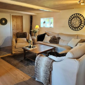 A living room with a wooden floor, a sofa, a chair, a coffee table, a wall clock, and a window with natural light. - Historic farmhouse from 1802 near Øster Hurup (Hadsund)