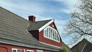 Un bâtiment rouge avec le numéro « 1802 » sur la façade, une entrée pavée et un jardin agrémenté de haies.