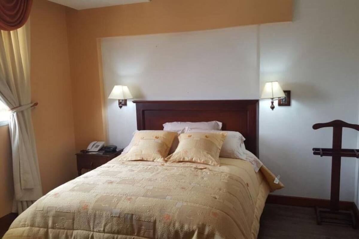 A hotel room with a bed, two bedside lamps, a nightstand, and a cross-shaped wall decoration.