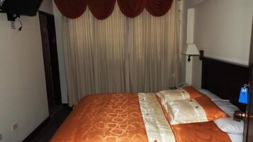 Una habitación de hotel con una cama, cortinas, un televisor montado en la pared y una lámpara.