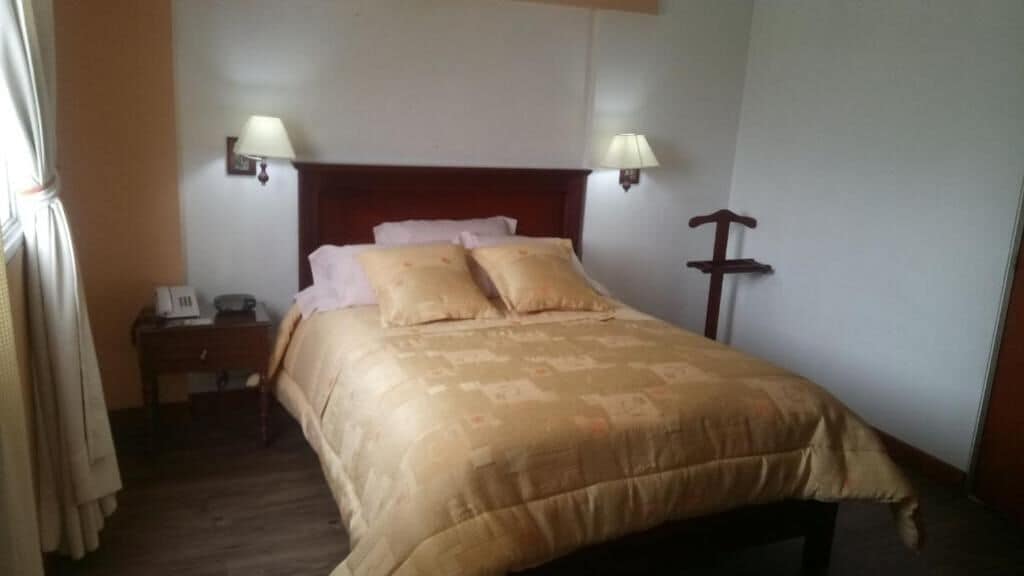 A bedroom with a bed, two bedside lamps, a nightstand, and a wooden headboard.