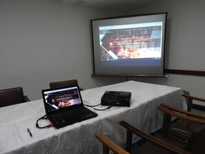 Ein Konferenzraum mit Laptop, Projektor und Präsentationsbildschirm, der eine Webseite zeigt.