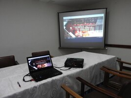 A conference room with a laptop, projector, and presentation screen displaying a website.