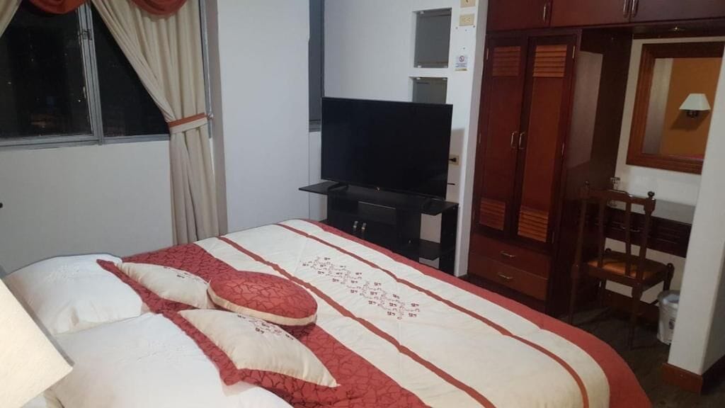 A bedroom with a bed, a television, a wardrobe, and a desk.