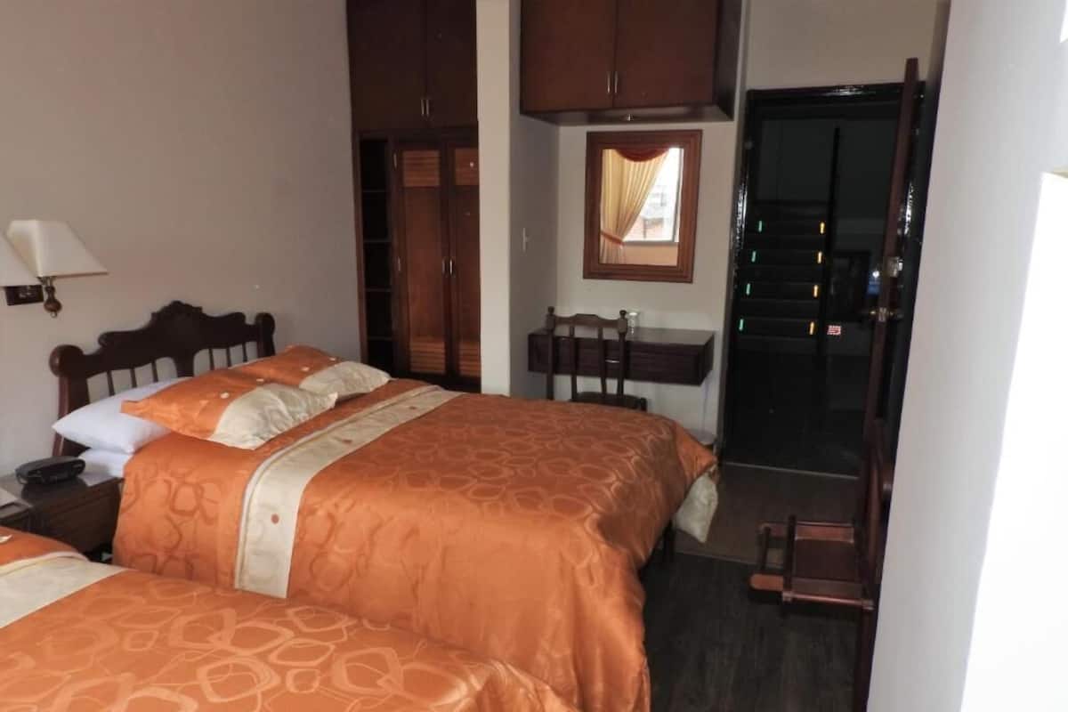 A hotel room with two beds, a desk, a chair, a window, and a door.