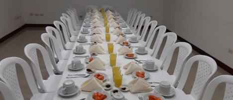 Una larga mesa de comedor con sillas blancas, dispuesta para una comida.