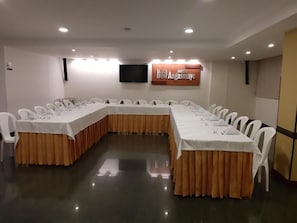 Ein Konferenzraum mit einem langen Tisch, weißen Stühlen und einem Fernsehbildschirm.