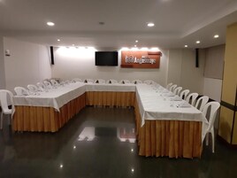 Uma sala de conferência com uma mesa comprida, cadeiras brancas e uma tela de televisão.