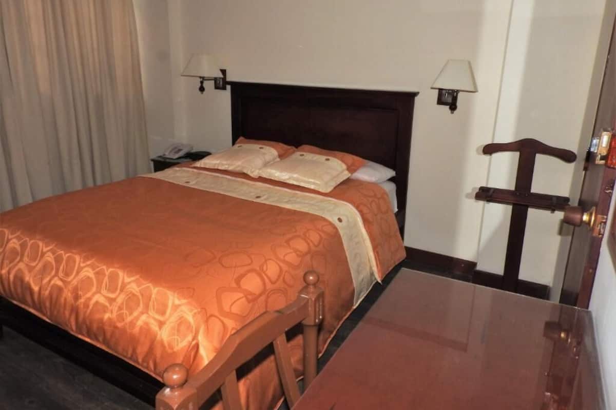 A hotel room with a bed, bedside lamps, a wooden nightstand, and a door.