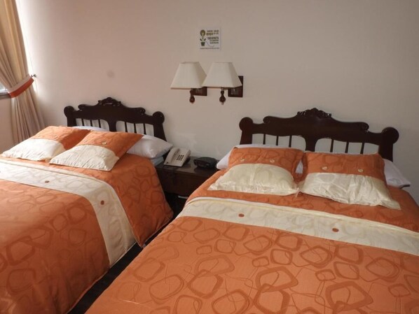 Two beds with matching headboards and pillows, a nightstand with a phone, and wall-mounted lamps. - Hotel Angasmayo (Ipiales)
