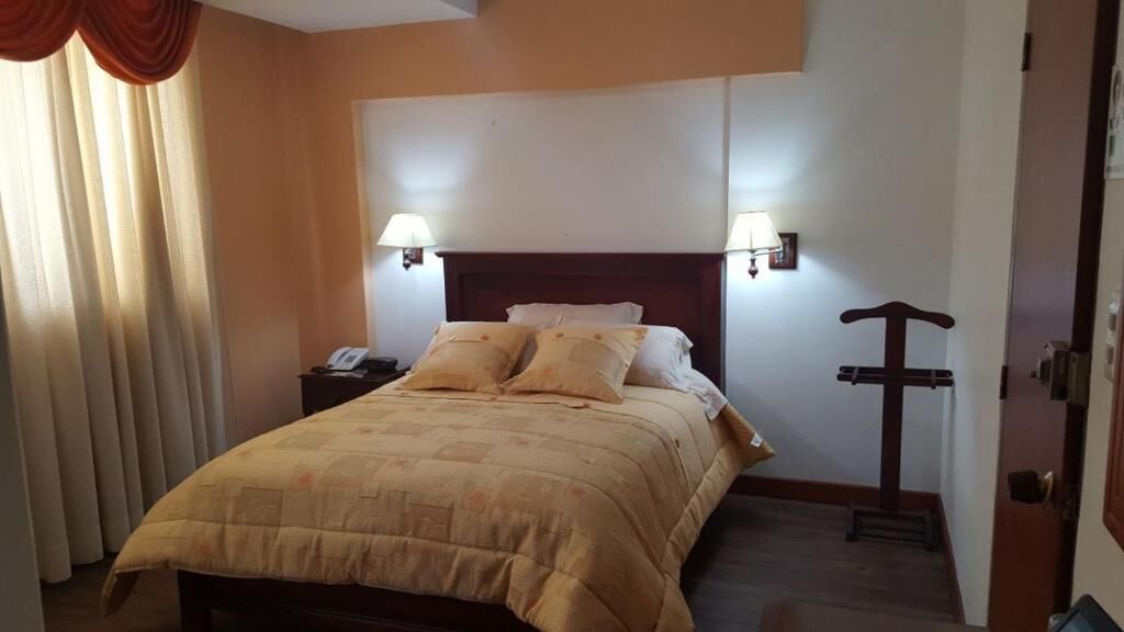 Una habitación de hotel con una cama, dos lámparas de noche, un teléfono y un perchero.