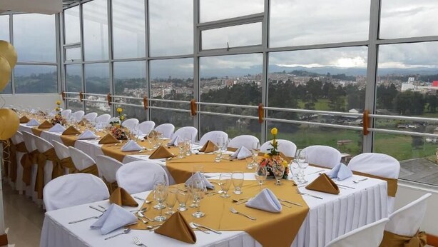 A banquet hall with tables set for a formal event, large windows offering a city view. - Hotel Angasmayo (Ipiales)