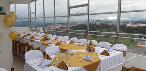 A banquet hall with tables set for a formal event, large windows offering a city view. - Hotel Angasmayo (Ipiales)
