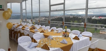 A banquet hall with tables set for a formal event, large windows offering a city view.