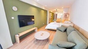 A modern living room with a flat-screen TV, a round coffee table, a sofa, and a bed with a white duvet. - The Colors of Larnaca (Larnaca)