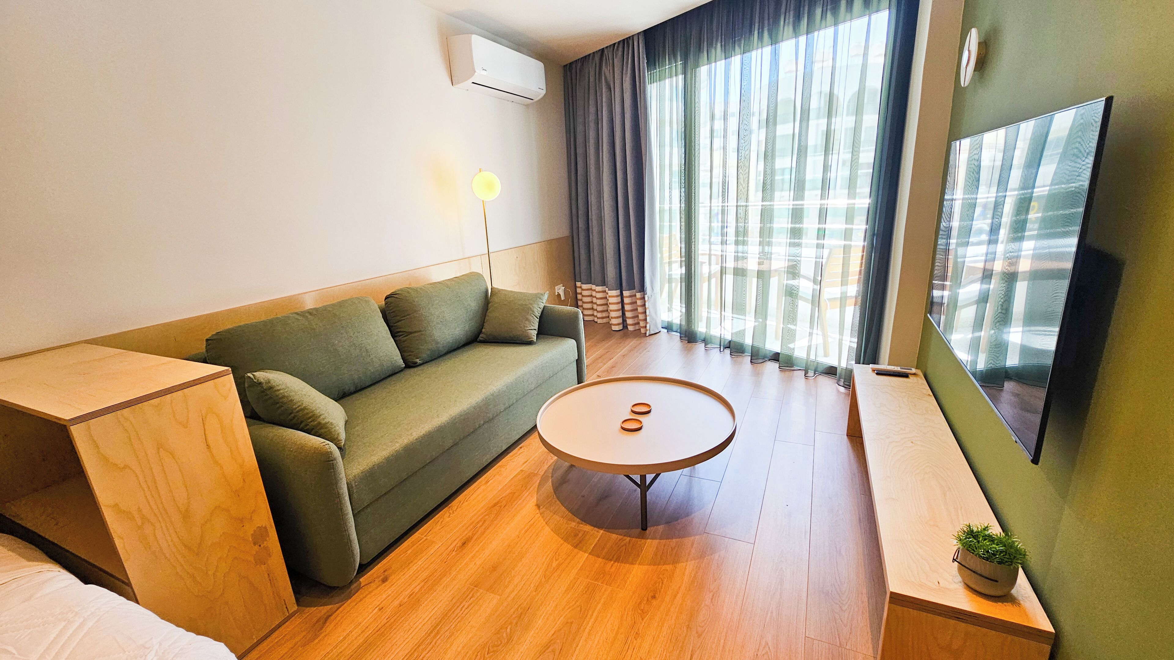 Una sala de estar moderna con un sofá, una mesa de centro, un televisor y una ventana con cortinas.
