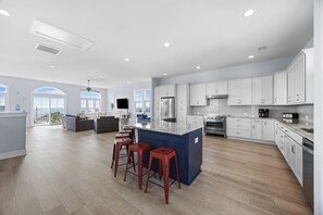 A spacious kitchen with a large island, bar stools, and modern appliances. - The Caddyshack at Carolina Beach (Carolina Beach)