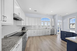 A modern kitchen with white cabinets, a granite countertop, and a large island. - The Caddyshack at Carolina Beach (Carolina Beach)