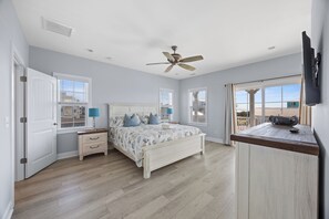 A bedroom with a bed, nightstands, a ceiling fan, and a TV mounted on the wall. - The Caddyshack at Carolina Beach (Carolina Beach)