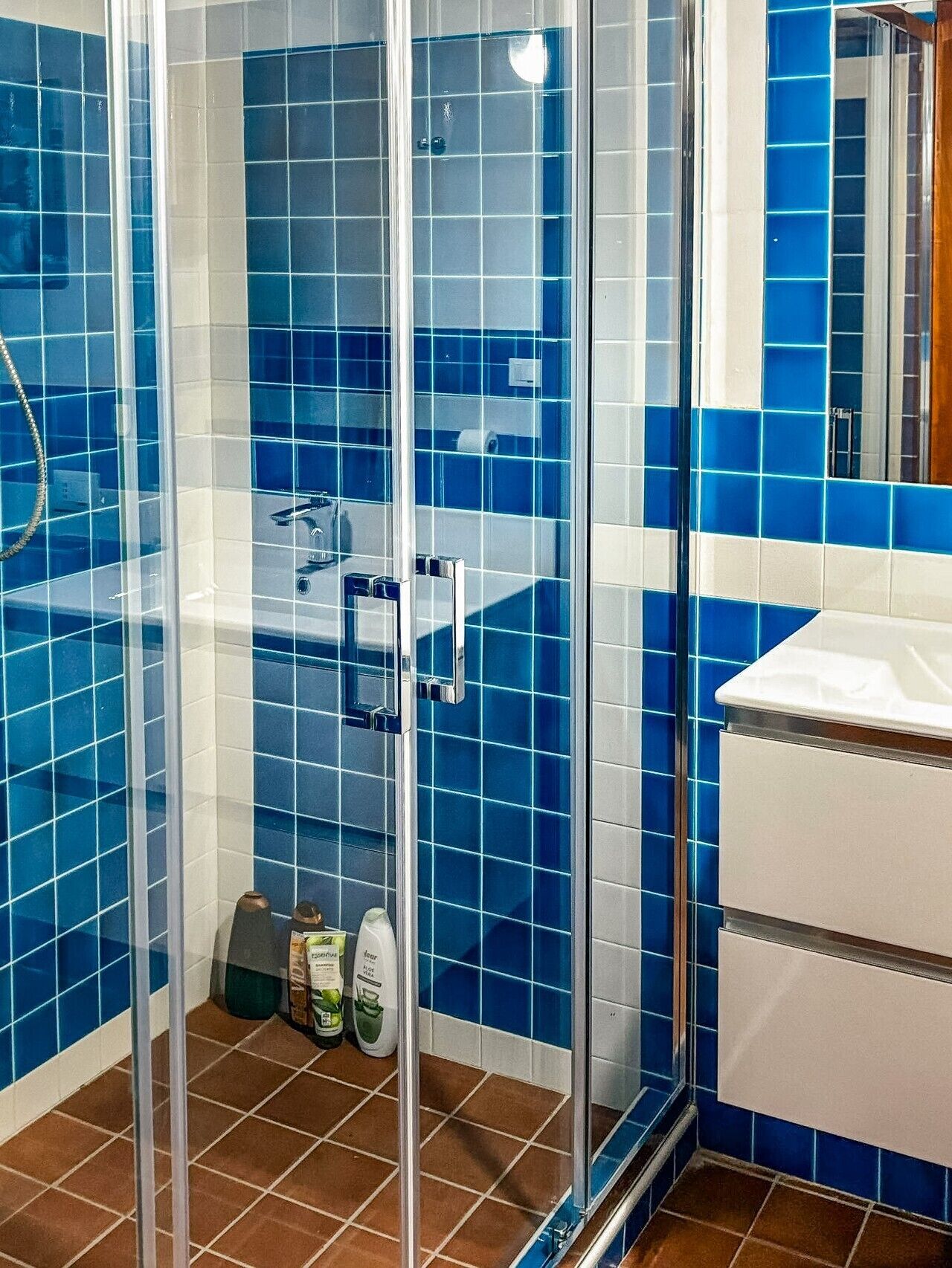 Ein Badezimmer mit blauen Fliesen, einer Duschkabine aus Glas und einem weißen Waschbecken.