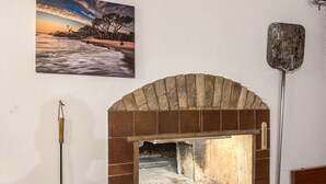 En tegelbeklädd öppen spis med ett metallgaller, en borste med träskaft och en metallspade som hänger på väggen.