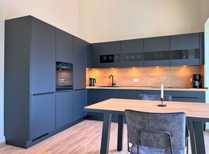 Eine moderne Küche mit dunklen Schränken, einem eingebauten Backofen, einer Holz Arbeitsplatte und einem Essbereich mit Tisch und Stühlen.