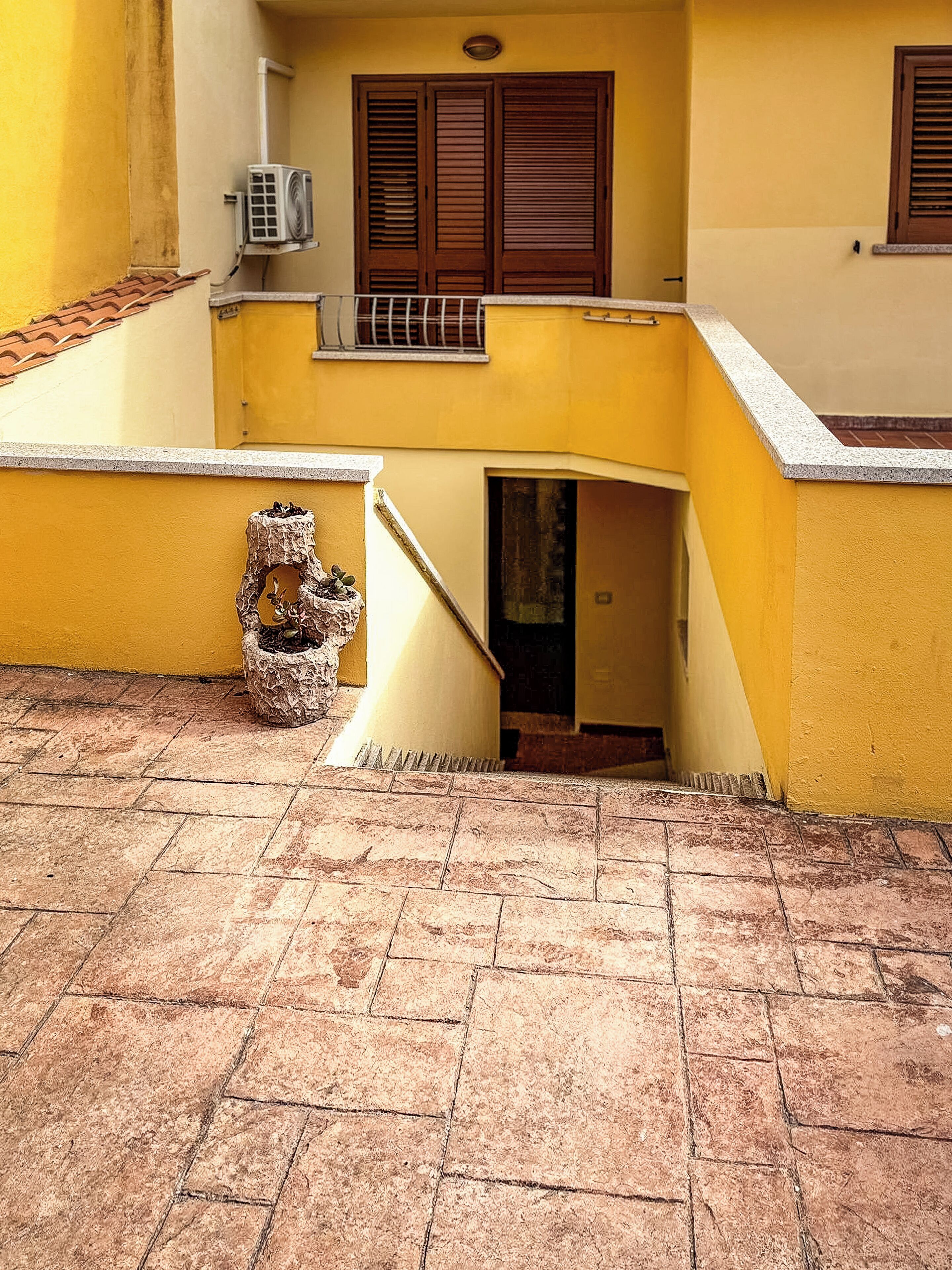 A yellow building with a tiled floor, a staircase, and a small balcony.