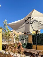 Un patio con mesa y sombrilla, rodeado de plantas y una valla.