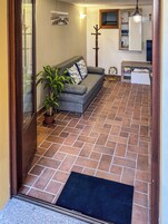 Una sala de estar con sofá, planta en maceta, perchero de madera y suelo de baldosas.