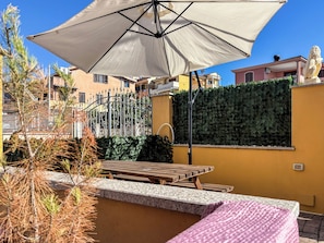 Un patio con una mesa y una sombrilla, una pared con seto verde y una estatua.