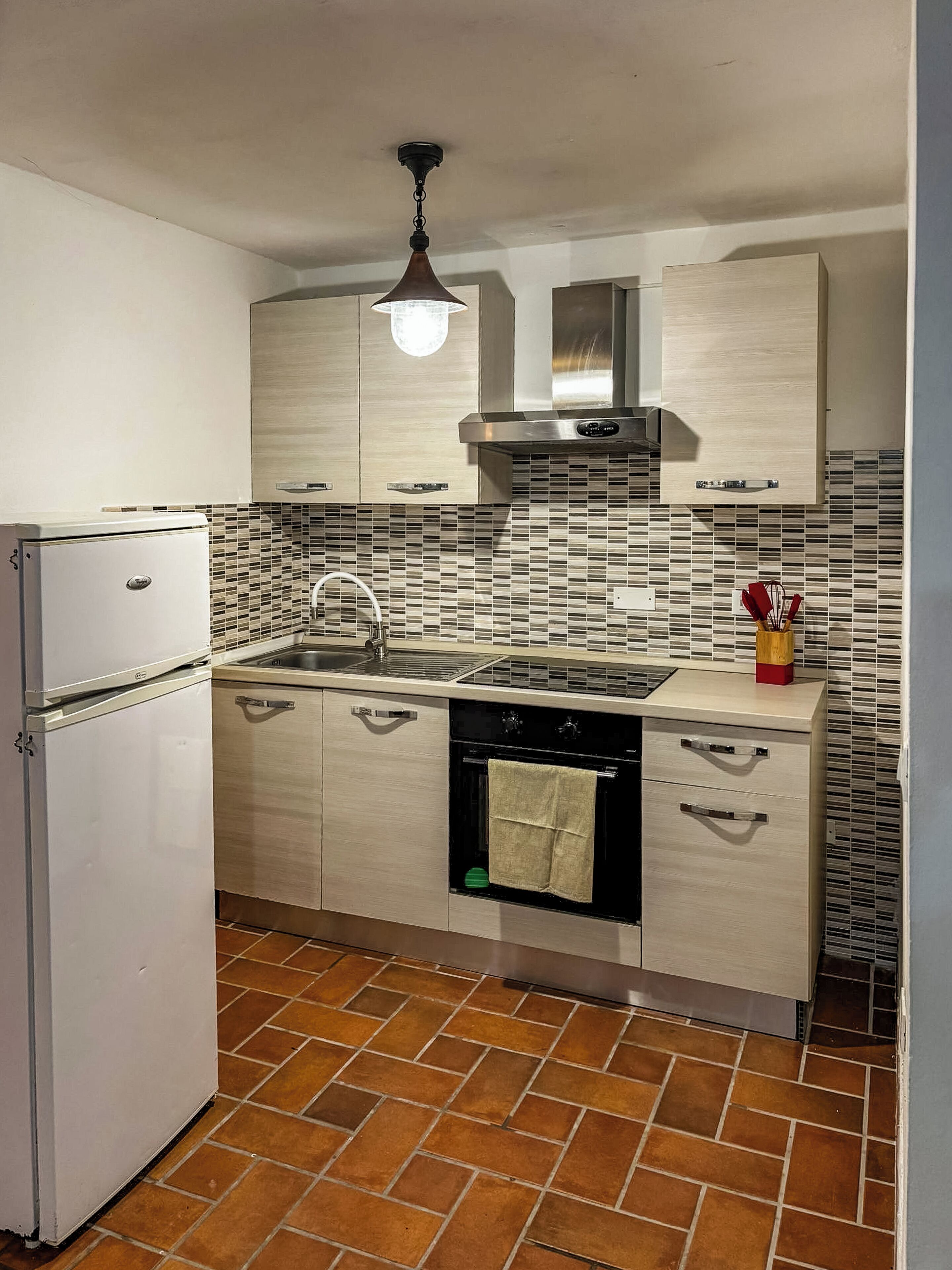 Una cocina compacta con refrigerador, estufa, lavaplatos y salpicadero de azulejos.