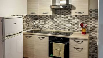 Una cocina compacta con refrigerador, estufa, lavaplatos y salpicadero de azulejos.