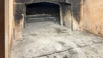 Un horno de piedra con una rejilla metálica en su interior, suelo de concreto y pared de ladrillo.